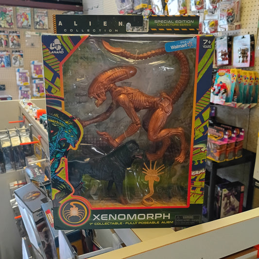 Xenomorph 7-inch action figure in its original retail packaging, displayed on a store shelf. The box features a clear window showing the brown Xenomorph figure and a black Alien Swarm figure, with colorful graphic borders.